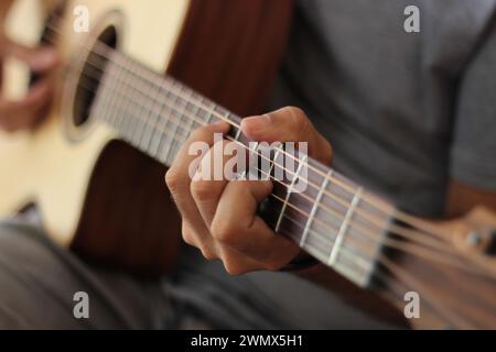 Eine Nahaufnahme fängt die emotionale Kunst der Hände ein, die eine akustische Westerngitarre spielen. Finger tanzen über das Griffbrett und überreden geschickt Melodien Stockfoto