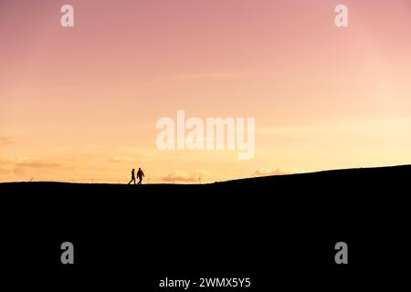 Ein Paar in der Ferne, das bei Sonnenuntergang vor der Kulisse des Himmels geschildert wurde Stockfoto