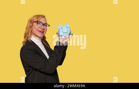 Glückliche Frau in schicker schwarzer Jacke, die Sparschweine entdeckt. Investitionen, Geld sparen, Geld Geld sparen, Geld einzahlen. Innenstudio isoliert aufgenommen Stockfoto