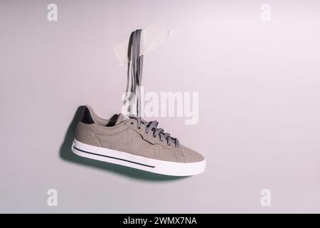 Graue Sneakers aus Stoff mit weißen Gummisohlen hängen an den Schnürsenkeln an der Wand Stockfoto