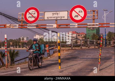 Ein Fahrer fährt mit seinem Motorrad durch den Eingang zur alten französischen Brücke auf dem Praek Tuek Chhu. Kampot, Kambodscha. © Kraig Lieb Stockfoto