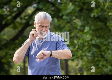 Aktiver männlicher Läufer, der seine Uhr während des Trainings im Freien betrachtet, konzentrierte sich auf Fitness und Zeitmanagement. Stockfoto