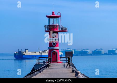 Großer Seefrachtkahn hinter dem roten Leuchtturm am Ende des Betonpiers in Donjin, Südkorea Stockfoto