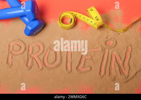 Wort-Protein geschrieben auf Proteinpulver auf rotem Hintergrund, mit Kurzhanteln und Maßband Stockfoto
