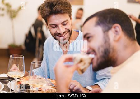 Zwei Männer lachen und essen mit Wein - Momente der Freundschaft und Freude bei einer zwanglosen Dinnerparty. Stockfoto