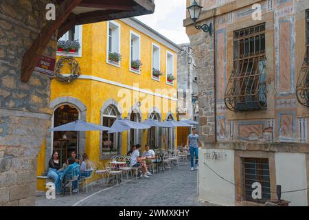 Viele Menschen sitzen vor historischen Gebäuden unter Sonnenschirmen in einer alten Stadtallee, Xanthi, Ostmakedonien und Thrakien, Griechenland Stockfoto