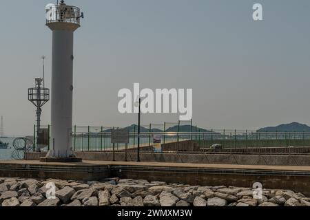 Weißer Leuchtturm am Ende des Betonpiers unter grauem bedecktem Himmel in Pyeongtaek, Südkorea Stockfoto