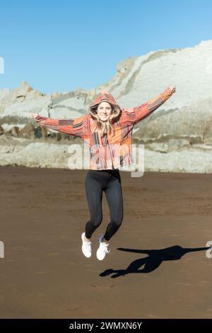 Eine hübsche blonde Frau, die am Strand nach Glück springt Stockfoto