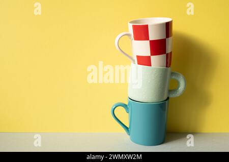 Stapel bunte Becher auf grauem Tisch. Gelber Wandhintergrund Stockfoto