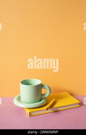 Notizbuch und Farbstift, Kaffeetasse auf rosa Schreibtisch. Orangefarbener Wandhintergrund. Arbeitsbereich Stockfoto