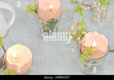 Frühling, Osterdekoration: Drei handgemachte Kerzen auf einem Tisch. Grüne Brunches. Nahaufnahme. Stockfoto