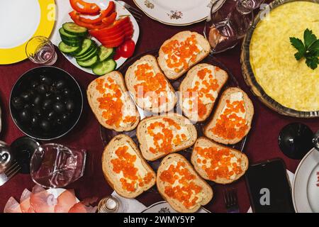 Ein wunderschön gedeckter Tisch mit hausgemachten Sandwiches mit rotem Kaviar, Butter, Oliven und frischem Gemüse, perfekt für festliche Anlässe wie ein bir Stockfoto