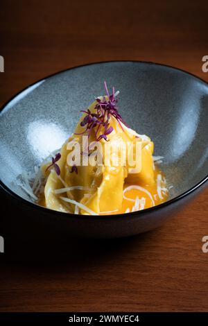 Tortellini aus Käse und Walnüssen, garniert mit geriebenem Käse und violettem Mikrogrün in einer dunklen Keramikschale. Stockfoto