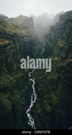 Von oben majestätische Aussicht auf einen kaskadierenden Wasserfall in Islands zerklüfteter Landschaft, umgeben von Nebel. Stockfoto