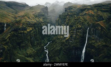 Von oben majestätische Aussicht auf einen kaskadierenden Wasserfall in Islands zerklüfteter Landschaft, umgeben von Nebel. Stockfoto