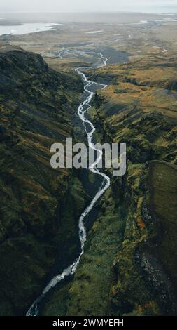 Von oben majestätische Aussicht auf einen kaskadierenden Wasserfall in Islands zerklüfteter Landschaft, umgeben von Nebel. Stockfoto