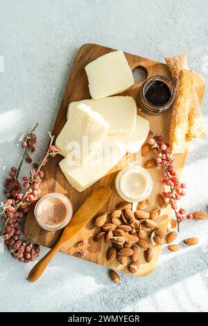 Eine Gourmet-Käseplatte mit verschiedenen Käsesorten, Mandeln, Honigwaben und Konserven auf einem rustikalen Holzbrett mit strukturierter heller Kulisse Stockfoto