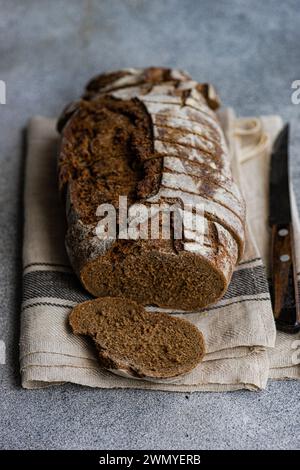 Geschnittenes Roggensauerteigbrot auf einem beigefarbenen Tuch mit einem Messer, das seine luftige Krume und das knusprige Äußere zeigt Stockfoto