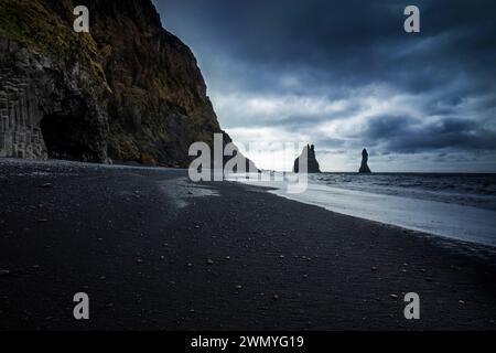 Eine stimmungsvolle isländische Küste unter dunklen Wolken, mit Basaltmeerestrukeln, die am Reynisfjara Beach den Horizont durchdringen. Stockfoto