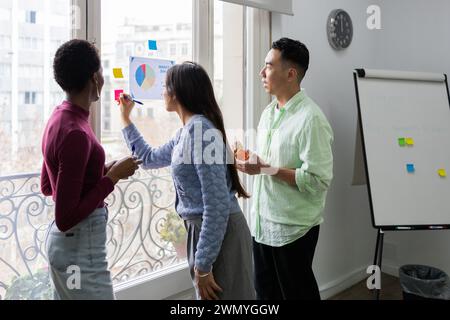 Ein vielseitiges Team arbeitet an einem Projekt zusammen und analysiert ein Tortendiagramm mit Marktanteilen in einer hellen Büroumgebung. Stockfoto