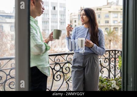Zwei Personen genießen gemeinsam eine entspannte Kaffeepause auf einem Balkon mit Blick auf die Stadt. Stockfoto