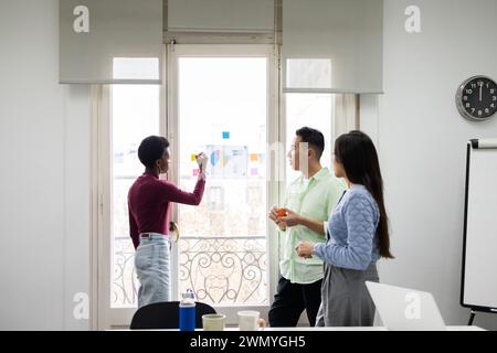 Drei Fachleute arbeiten in einem hellen Büro zusammen und diskutieren während eines Geschäftstreffens ein farbcodiertes Marktanteilsdiagramm Stockfoto
