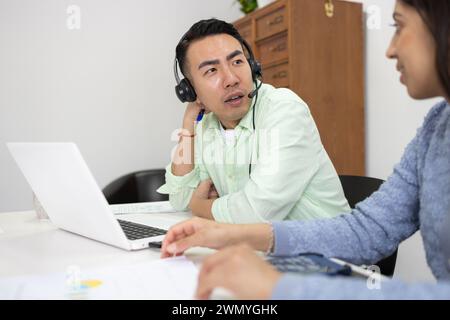 Zwei Fachleute führten ein Gespräch mit einem Laptop auf einem weißen Schreibtisch in einer gut beleuchteten Büroumgebung. Stockfoto