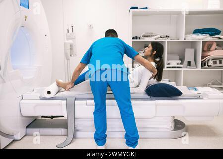 Ein medizinisches Fachpersonal wird dabei gesehen, wie er einem Patienten in einem hellen klinischen Umfeld bei einem MRT-Scanner hilft. Stockfoto