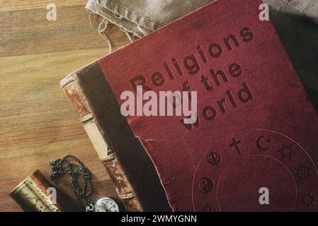 Detail des alten Buches über das Studium der Religionen in der Welt mit graviertem Text und Symbolen verschiedener Religionen auf Holztisch mit dekorativen Objekten. Stockfoto