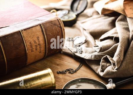 Altes und verschlechtertes Buch der Religionen der Welt mit alten Studien- und Abenteuergegenständen auf Holztisch. Erhöhte Aussicht. Stockfoto