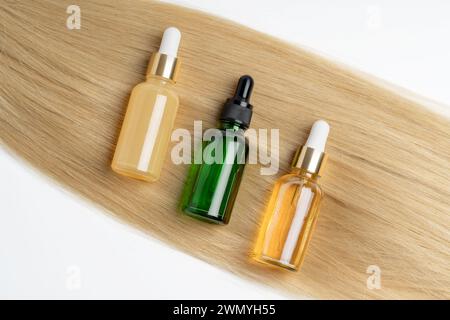 Drei verschiedene Flaschen mit ätherischem Öl auf einer Strähne blondes Haar für Haarpflege und Kosmetik. Stockfoto