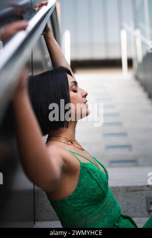 Seitenansicht eines modernen Modeporträts mit einer jungen Frau in einem leuchtend grünen Kleid und Madrids ikonischem Geschäftsviertel Cuatro Torres im Hintergrund Stockfoto