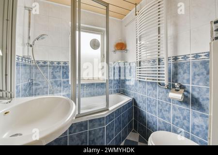 Ein gut beleuchtetes Badezimmer mit blauen Fliesen, Duschkabine, Toilette und beheiztem Handtuchhalter. Stockfoto