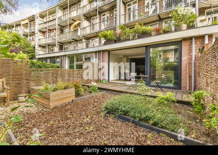 Moderne Apartmentterrasse mit Glastüren, Sitzgelegenheiten im Freien und einem üppigen Garten, eingebettet zwischen städtischen Wohngebäuden. Stockfoto