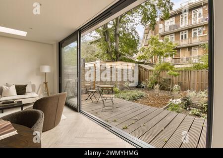 Ein gemütliches, modernes Wohnzimmer verbindet sich durch große Glasschiebetüren nahtlos mit einem ruhigen Garten und bietet einen ruhigen Wohnbereich im Innen- und Außenbereich. Stockfoto