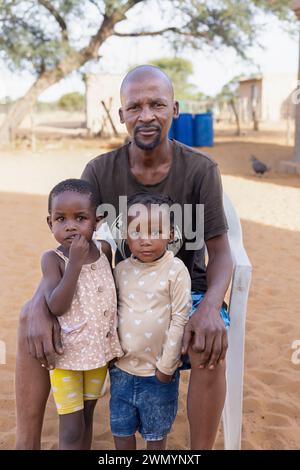 Das afrikanische Dorf saß zusammen mit zwei seiner Töchter auf einem Stuhl im Hof Stockfoto