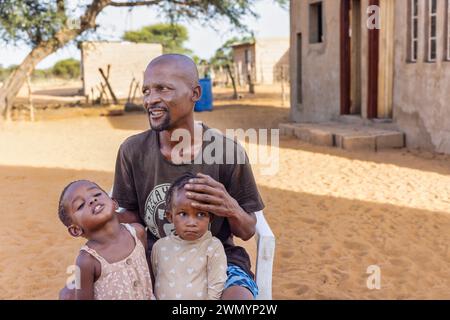 Das afrikanische Dorf saß zusammen mit zwei seiner Töchter auf einem Stuhl im Hof Stockfoto