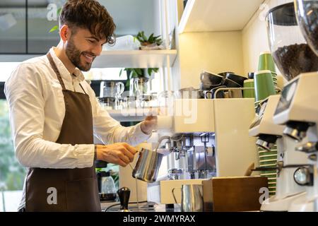 Lächelnder Mann Barista, der Kaffee im Café brütet, lächelt glücklich Stockfoto