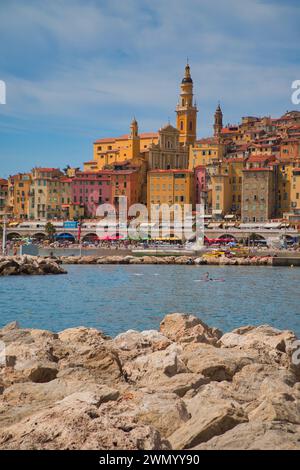 Menton, Frankreich - August 5,2021: Panoramablick auf die farbenfrohe Altstadt Menton und die Einheimischen genießen Wasseraktivitäten im Meer an einem heißen Sommertag in french R Stockfoto