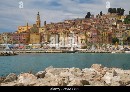 Menton, Frankreich - August 5,2021: Panoramablick auf die farbenfrohe Altstadt Menton und die Einheimischen genießen Wasseraktivitäten im Meer an einem heißen Sommertag in french R Stockfoto