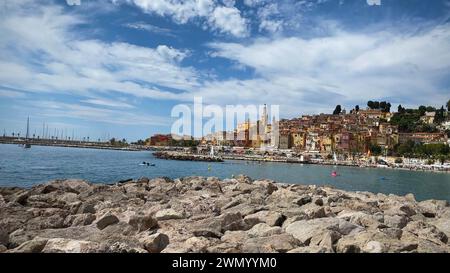 Menton, Frankreich - August 5,2021: Panoramablick auf die farbenfrohe Altstadt Menton und die Einheimischen genießen Wasseraktivitäten im Meer an einem heißen Sommertag in french R Stockfoto