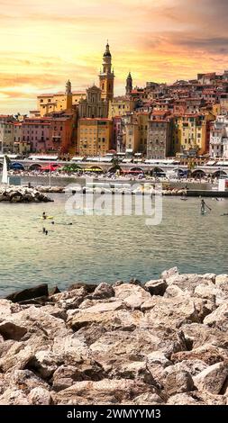 Menton, Frankreich - August 5,2021: Panoramablick auf die farbenfrohe Altstadt Menton während des Sonnenuntergangs und Einheimische genießen Wasseraktivitäten im Meer in einem heißen Sommer Stockfoto