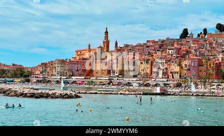 Menton, Frankreich - August 5,2021: Panoramablick auf die farbenfrohe Altstadt Menton und die Einheimischen genießen Wasseraktivitäten im Meer an einem heißen Sommertag in french R Stockfoto