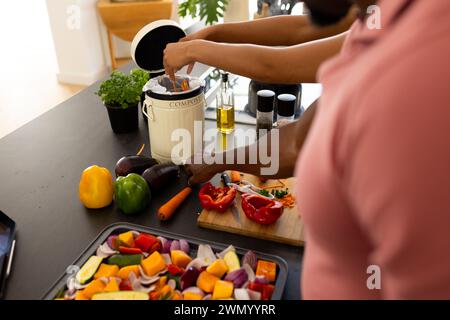 Ein Afroamerikaner fügt Essensreste in einen Kompostbehälter in einer Küche zu Hause Stockfoto