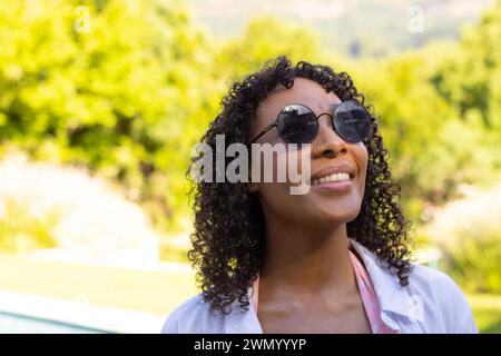 Eine junge Frau mit Sonnenbrille lächelt draußen zu Hause Stockfoto