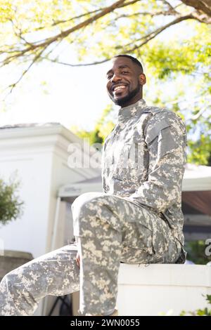 Ein afroamerikanischer Soldat in Militäruniform sitzt lächelnd unter einem Baum Stockfoto