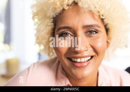 Eine junge Frau mit lockigen blonden Haaren lächelt warm und trägt ein hellrosa Hemd Stockfoto