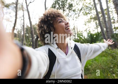 Eine junge Frau mit lockigen Haaren macht ein Selfie im Wald auf einer Wanderung Stockfoto