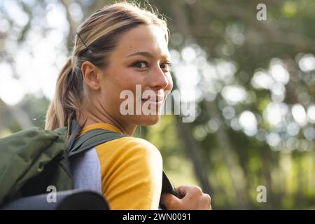 Eine junge kaukasische Frau mit blonden Haaren schaut zurück, lächelnd, auf einer Wanderung Stockfoto