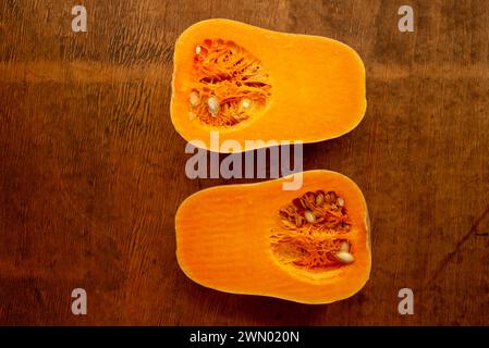 Zwei Hälften geschnittener reifer Butternusskürbis mit Samen auf rustikaler Holztischplatte von oben Stockfoto
